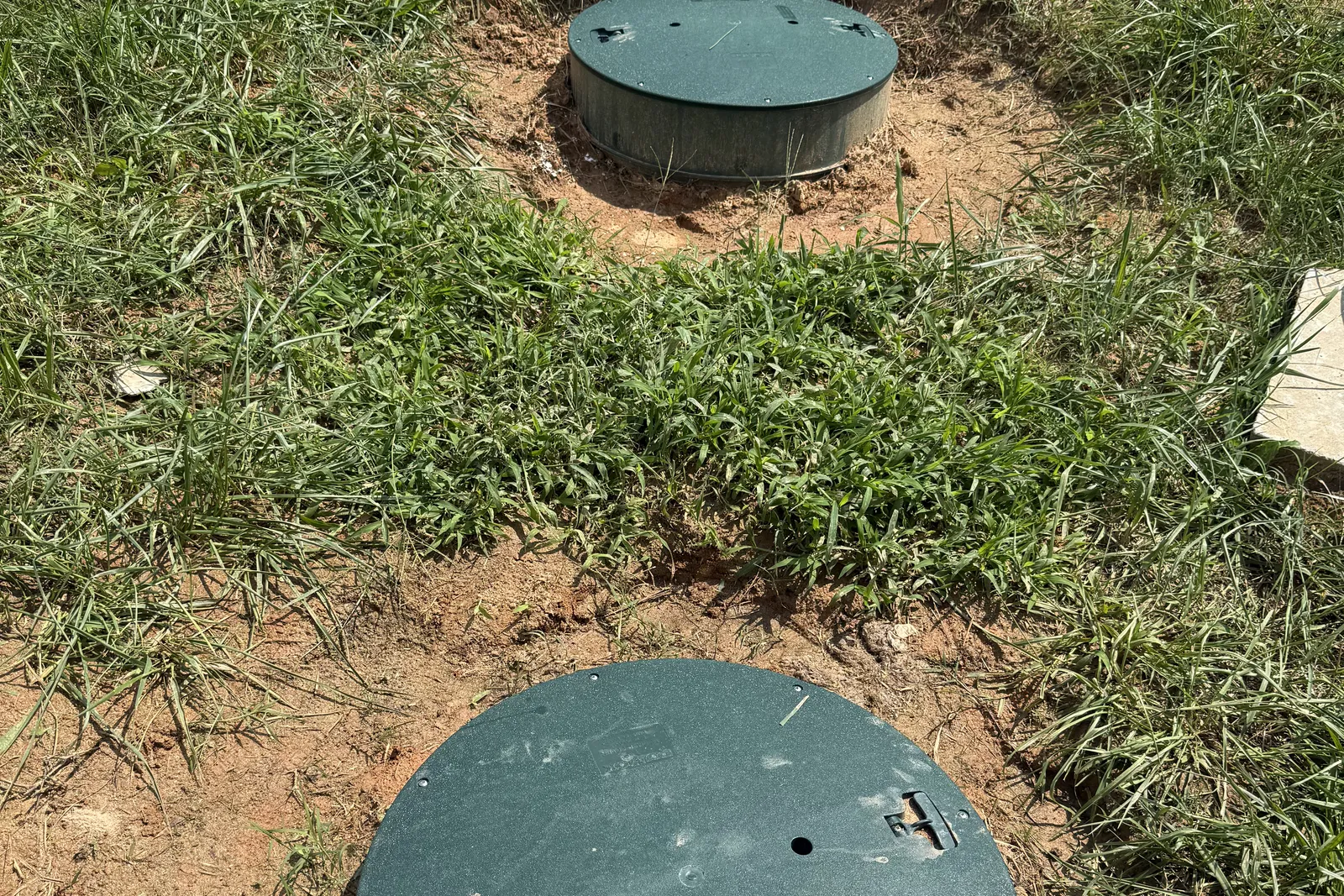 Two finished septic riser lids sitting at ground level in intact grass